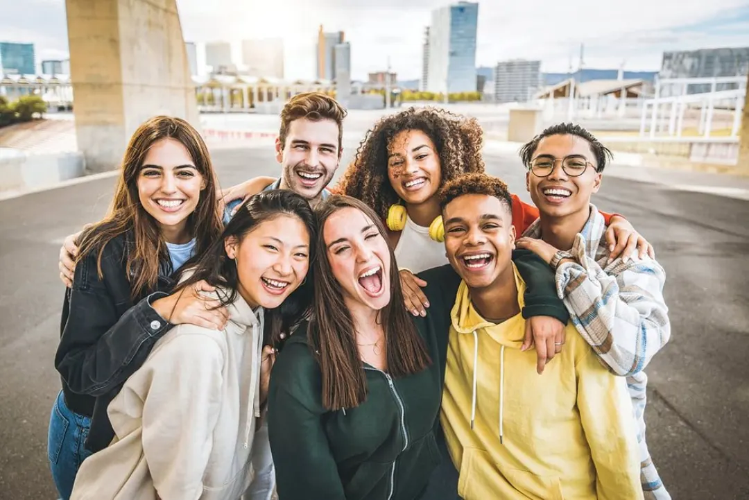 Gen Z jenerasyonu: şehir manzarası önünde birbirine sarılıp gülen genç grup
